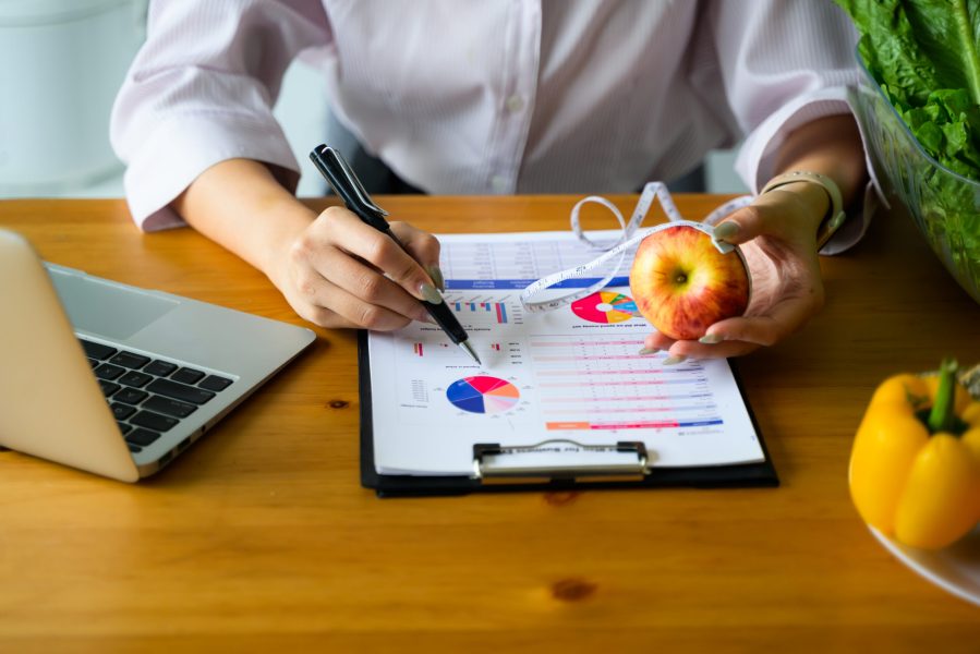 Nutritionist calculating and recommending healthy diet meals for wellness on a wooden desk